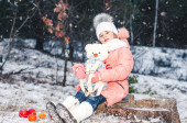 Vtipná holčička v zimě zasněžený novoroční les hraje s hračkou bílého medvěda. Zimní portrét dítěte.