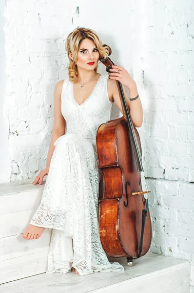 Cello music instrument orchestra player cellist playing classic. Closeup of cello with bow in hands. A blonde girl holding a cello, playing, smiling.