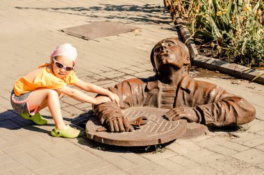 Yaz parkında güneş gözlüklü mutlu küçük kız komik bir tesisatçı heykelinin yanında.