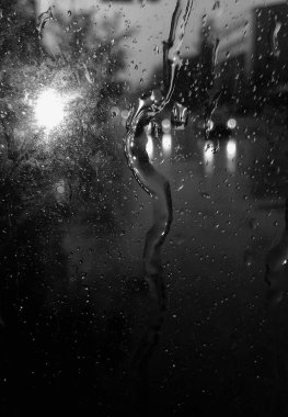 Araba camına yağmur damlaları düşer, yağmur damlalarına odaklanır. Siyah beyaz fotoğraf.