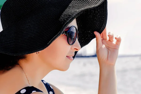 海を背景にサングラスをかけ黒い帽子を被った美しい少女の肖像画 — ストック写真