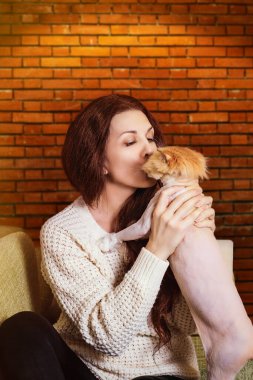 Genç, güzel, kızıl saçlı bir kadın yeşil bir kanepeye oturur ve şeftali rengi bir İran kedisiyle oynar..