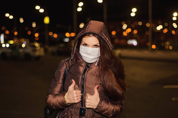 Karantina sırasında onu akşam sokağında virüsten koruyacak tıbbi maskeli bir kadın. Koronavirüs salgını. Maskeli kadın ayakta. İnsanlar hastaneye kaldırılıyor, teşhis konuyor, belirtileri gösteriyor..