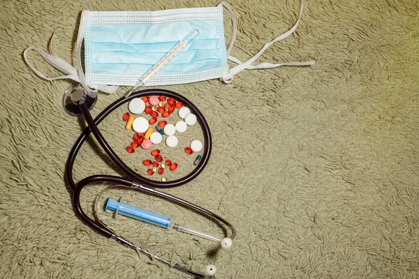 Protective mask, medicines, thermometer, stethoscope and syringe with coronavirus text on a green tissue background. Novel coronavirus 2019-nCoV, MERS-Cov middle East respiratory syndrome coronavirus.