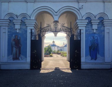 Grand gates of monastery in Russia. Saints on walls and church in background.