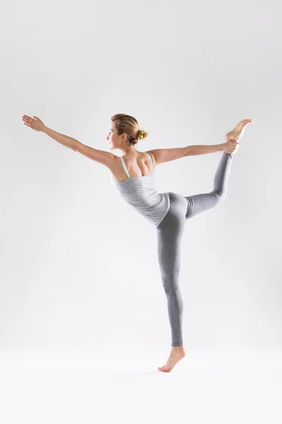 Vacker ung kvinna gör yoga på en grå studio bakgrund — Stockfoto