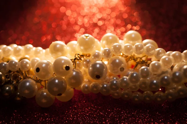 Primer plano de perlas blancas sobre un fondo de purpurina roja . — Foto de Stock