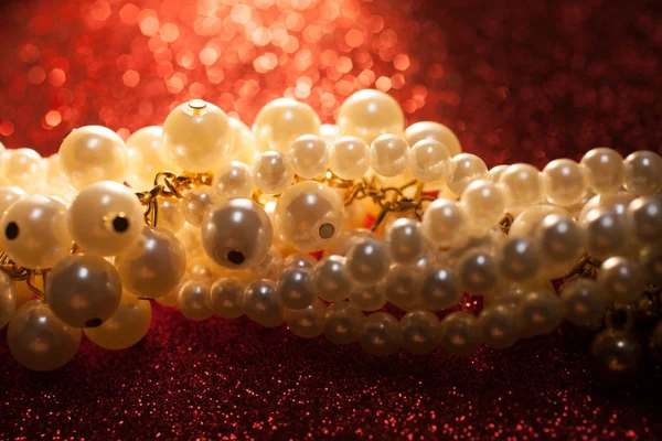 Zbliżenie na białe perły na tle czerwonym brokatem. — Zdjęcie stockowe