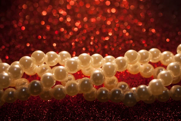 Close up of white pearls on a red glitter background.
