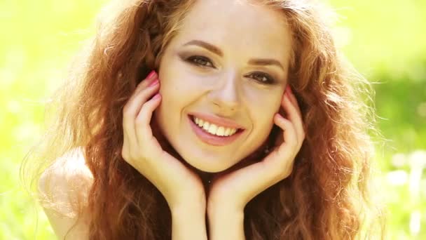 Krásy dívka s dlouhými kudrnatými vlasy zdravé venku. Šťastný usměvavá mladá žena padají na trávě.