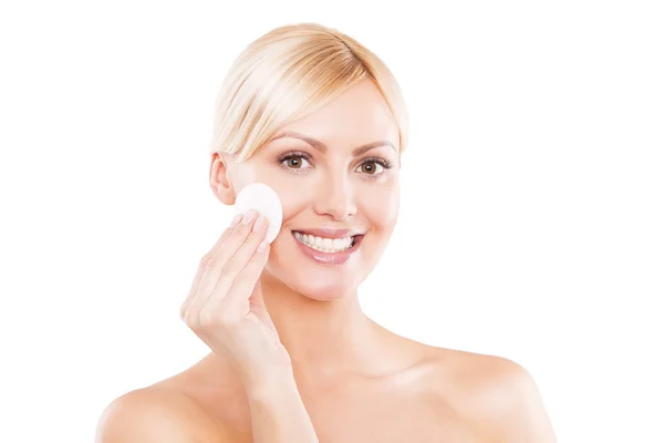 Photo d'une femme blonde heureuse nettoyant son visage avec des tampons de coton sur fond blanc — Photo