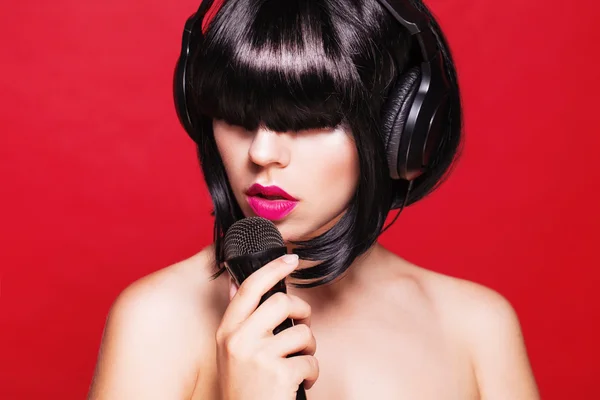 Detailní portrét krásné ženy s mikrofonem. Karaoke. na červeném pozadí — Stock fotografie