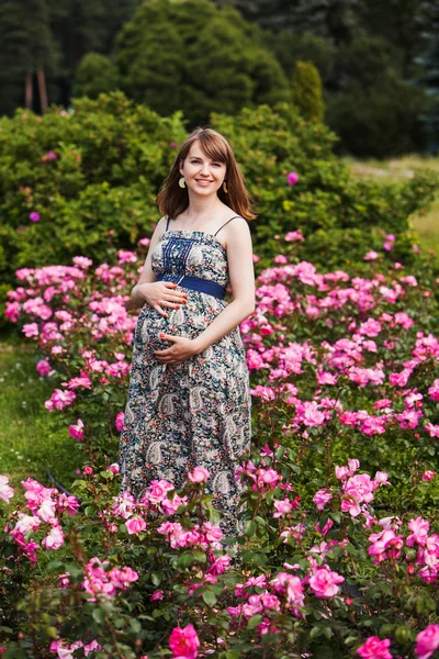 Szép terhes nő mosolyogva. kültéri. a háttérben a virágok — Stock Fotó