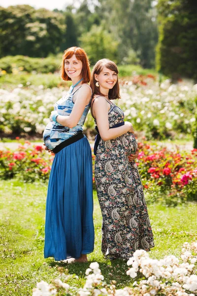 Zwei schöne, glückliche schwangere Freundinnen. Draußen. vor dem Hintergrund der Blumen — Stockfoto