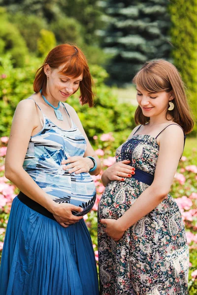 Två vackra glada gravida kvinnor. utomhus. mot bakgrund av blommor — Stockfoto