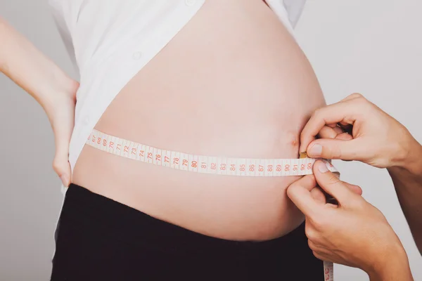 Vientre de una mujer embarazada con cinta métrica, 9 meses —  Fotos de Stock