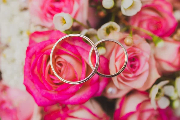 Vigselringar på en bukett rosa, röda blommor — Stockfoto