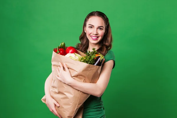 Mulher bonita segurando um saco de supermercado cheio de alimentos frescos e saudáveis. sobre fundo verde — Fotografia de Stock