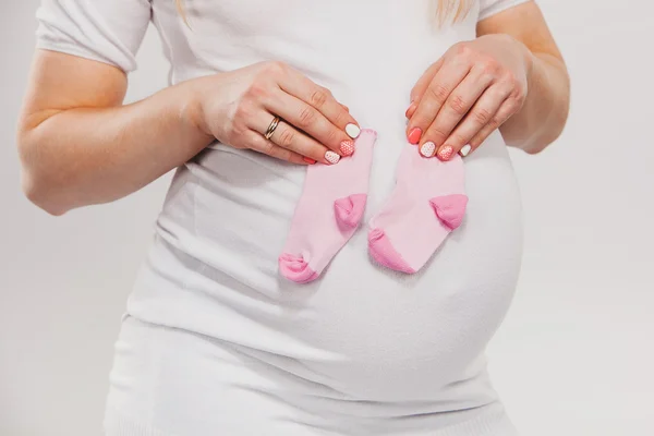 Mulher grávida com dois tipos de meias para o futuro bebê - fundo branco. Maternidade e novo conceito de família — Fotografia de Stock