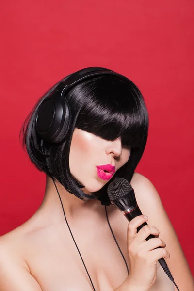 Chica elegante cantando con un micrófono, fondo rojo. Karaoke — Foto de Stock