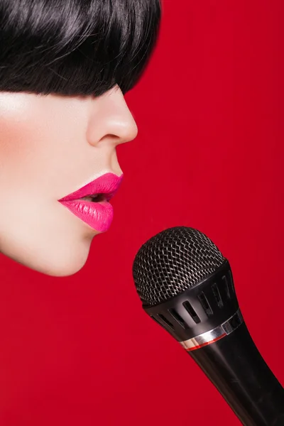 Elegante modelo de mujer con un micrófono, fondo rojo. Karaoke — Foto de Stock