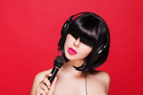 Chica elegante cantando con un micrófono, fondo rojo. Karaoke — Foto de Stock