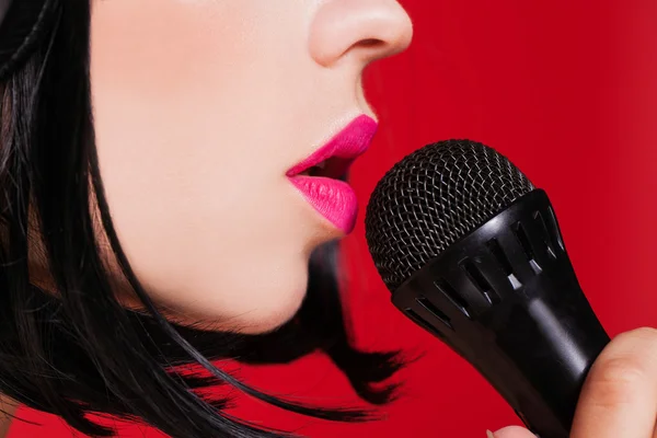 Karaoke. Linda jovem modelo cantando com um microfone no fundo vermelho . — Fotografia de Stock