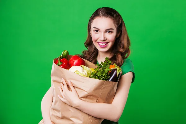 新鮮で健康食品の食料品袋を保持する美しい若い女性。緑の背景 — ストック写真