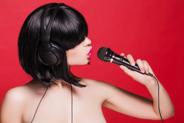 Chica elegante cantando con un micrófono, fondo rojo. Karaoke — Foto de Stock