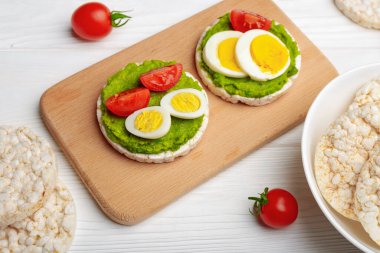 Avokado ezmeli pirinç kekleri ve tahta kesme tahtasında domatesli yumurtalar ve beyaz ahşap arka plan..