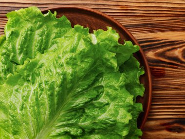 Ahşap arka planda bir kasede yeşil marul yaprakları.