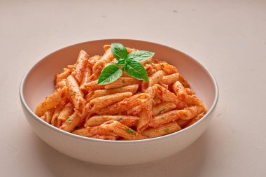Close-up of a plate with Penne All'arrabbiata pasta cooked according to a traditional Italian recipe on a light background