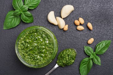 Fesleğen soslu cam kavanoz ve koyu arkaplanda malzemeler.