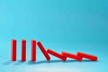 A series of red rectangular dominoes stands upright, with the first few tipping over and creating a chain reaction. copy space