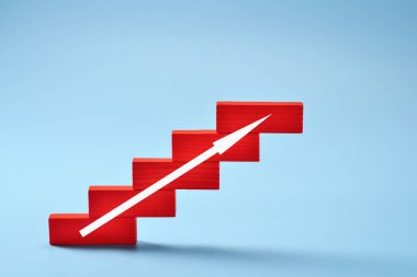 Tahta bloklar, açık mavi bir zemine karşı merdiven basamağı şeklinde dizilmiş. Yükselen bir ok kariyer büyüme kavramındaki ilerlemeyi gösterir ve başarıyı simgeler..