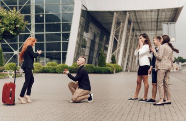Arkadaşlarıyla birlikte bir adam havaalanında kız arkadaşını bavuluyla karşılar. Genç bir adam güzel kızıl saçlı bir kıza evlenme teklif ediyor. Adam elinde yüzükle tek dizinin üstünde duruyor..