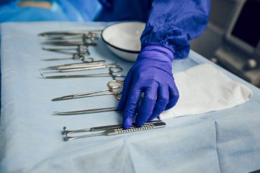 Masanın üstündeki ameliyathanede cerrahi aletleri yerleştiren mavi bir eldiven verin. Ameliyat için hazırlık. Steril aletler.
