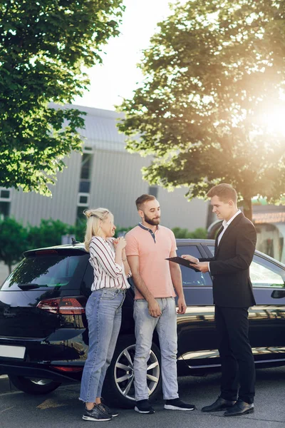 행복 한 부부가 새 차를 삽니다. 자동차를 구입 한 젊은 부부를 맞이하는 남성 판매원 — 스톡 사진