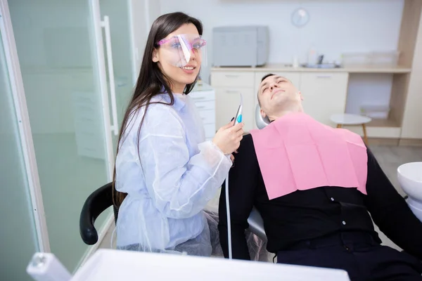 Un homme assis sur une chaise dentaire, avec un mal de dents. Une dentiste assise près d'un patient tenant un outil — Photo