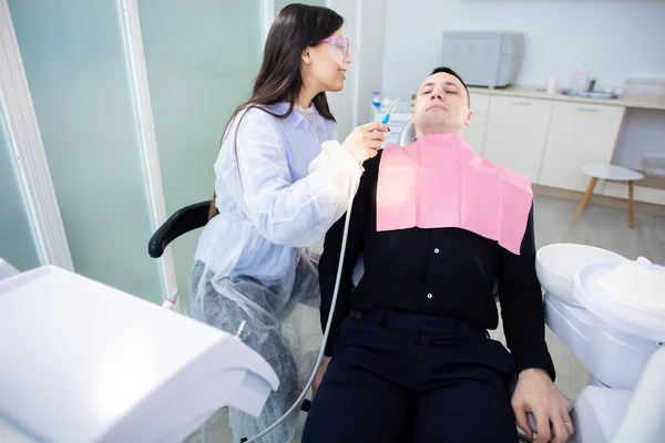 La dentista femenina examina a un paciente masculino. Hombre joven en la silla de dentistas durante un procedimiento dental. Sonrisa saludable — Foto de Stock