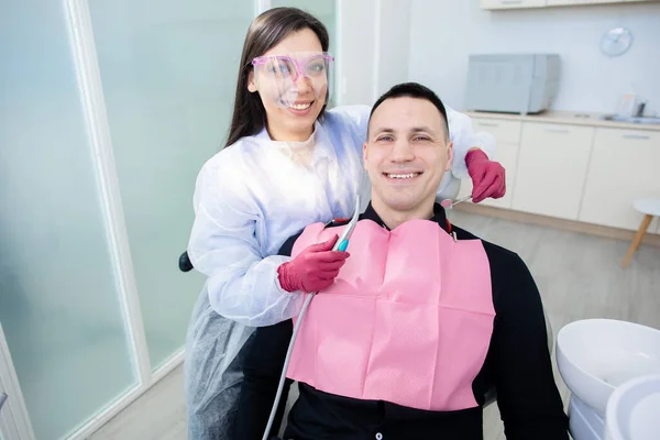 Vrouwelijke tandarts onderzoekt een mannelijke patiënt. Jongeman in de tandarts stoel tijdens een tandheelkundige ingreep. Gezonde glimlach — Stockfoto