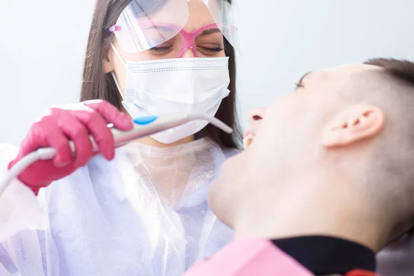 Close up view of dental caries prevention. Female dentist examines a male patient. Young man in the dentists chair during a dental procedure — Stock Photo, Image