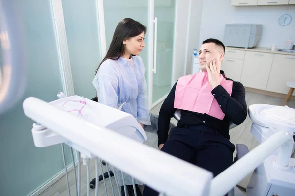 A man sitting in a chair, with a toothache. Young female dentist listens to patient complaints — Stock Photo, Image