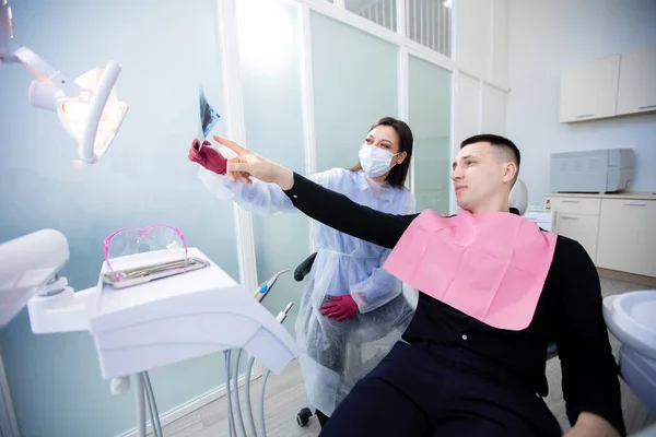 La dentista mostra una radiografia a un paziente di sesso maschile. Giovane dal dentista — Foto Stock