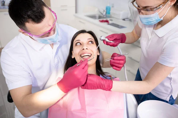 Young smiling woman in a dental chair. Two dentists check the teeth and do their hygiene. Healthcare, medicine — Stock Photo, Image