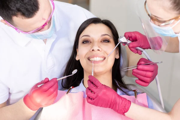 Dişçi koltuğunda gülümseyen genç bir kadının portresi. İki dişçi dişlerini kontrol eder ve hijyenlerini kontrol eder. Sağlık, ilaç. — Stok fotoğraf