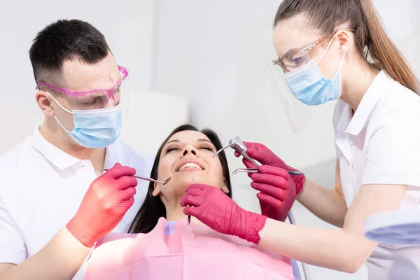 Two dentists treat the teeth of a young patient. Woman sitting in a dental chair. Healthcare, medicine — Stock Photo, Image