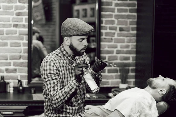 Jovens numa barbearia. O cabeleireiro desinfeta a navalha e a tesoura antes de raspar a barba dos clientes. — Fotografia de Stock