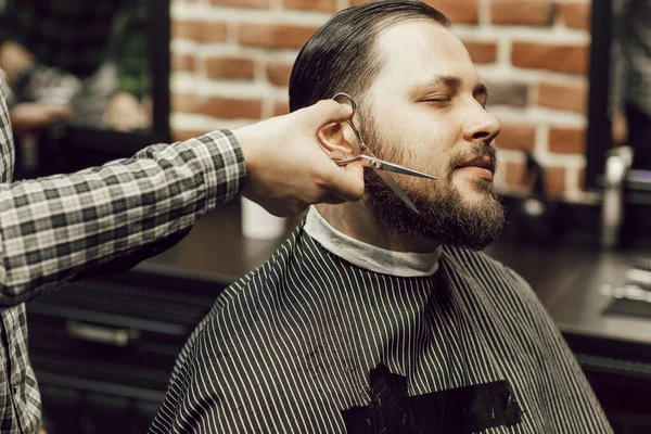 Um homem de perto corta a barba dos clientes com uma tesoura. Corte de cabelo em uma barbearia — Fotografia de Stock