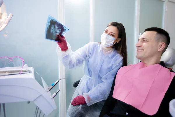 La dentista mostra una radiografia a un paziente di sesso maschile. Un uomo nello studio dentistico, prevenzione della carie — Foto Stock